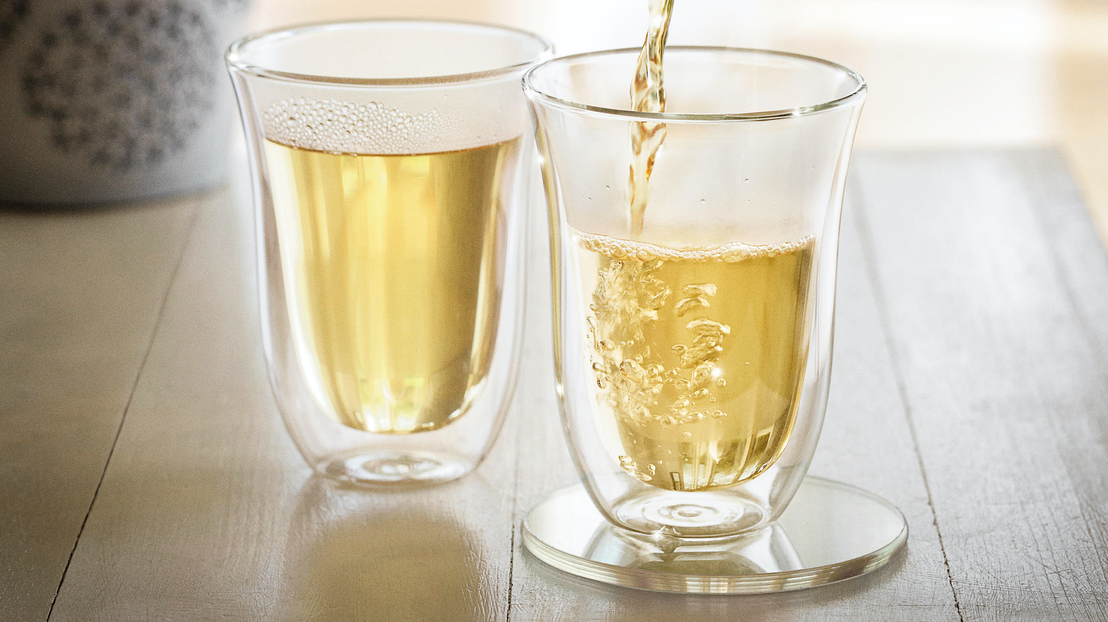 A glass containing tea being poured into another glass.