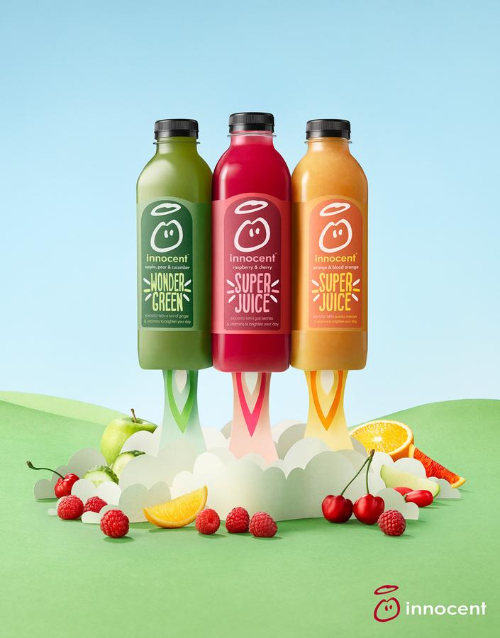 Three bottles of juice, one green, one red, and one orange, with various fruits and fruit-juice-related items in the background.