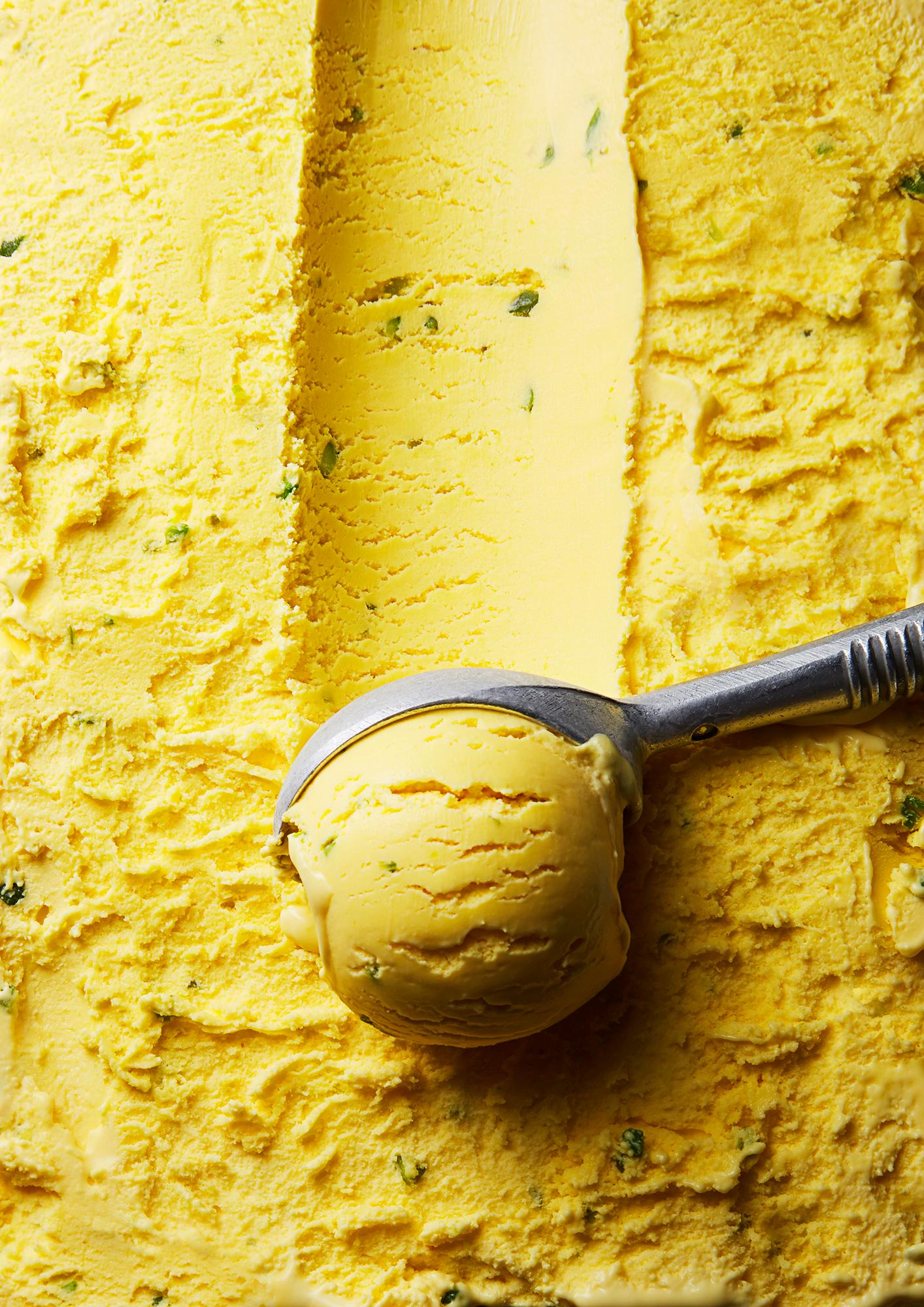 A scoop of yellow ice cream with a metal scoop in a metal container.