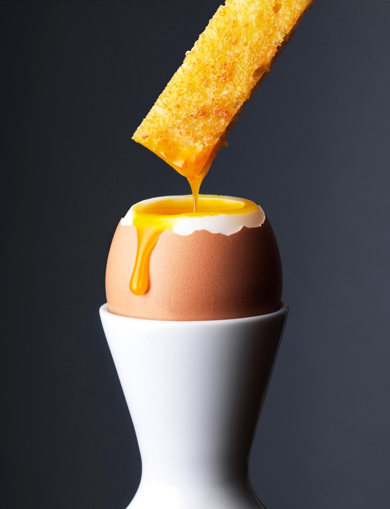 A fried egg being poured onto a toasted slice of bread, with a golden, runny yolk.
