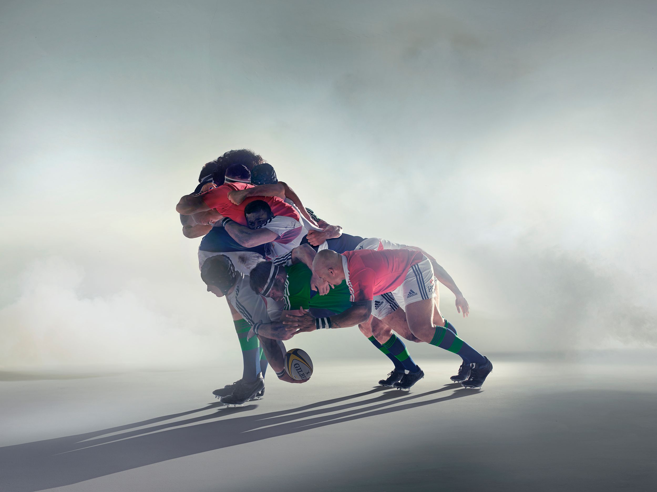 A group of rugby players in various positions, including tackling, running, and falling, in a dynamic and action-packed scene.