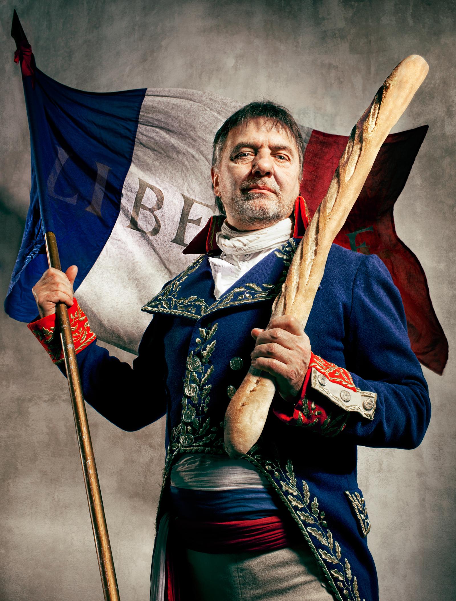 A man in a 19th-century French military uniform holds a baguette and a tricolor flag with 'Liberté' written in French.