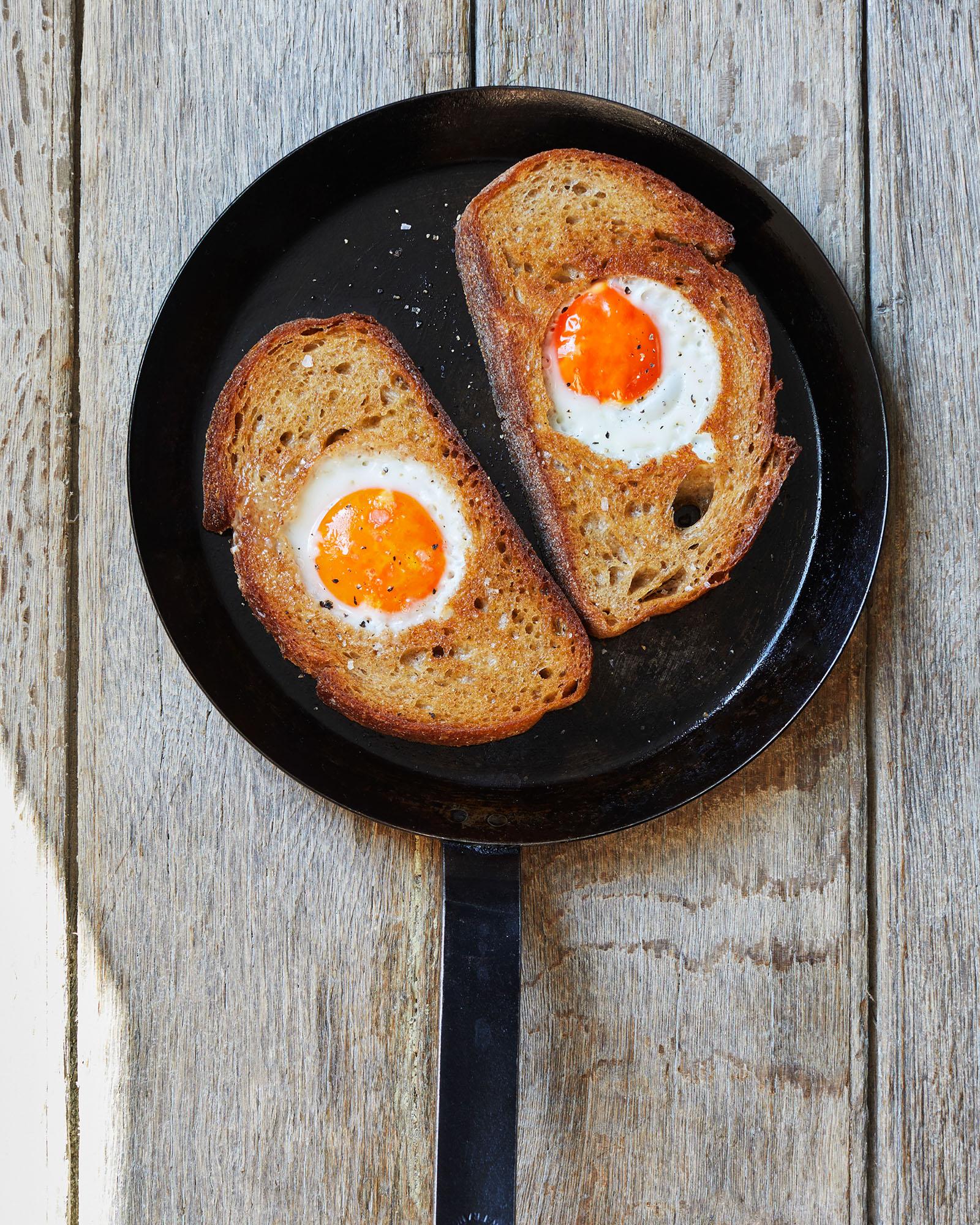A toasted bread slice with a fried egg in the center, served in a cast-iron skillet.