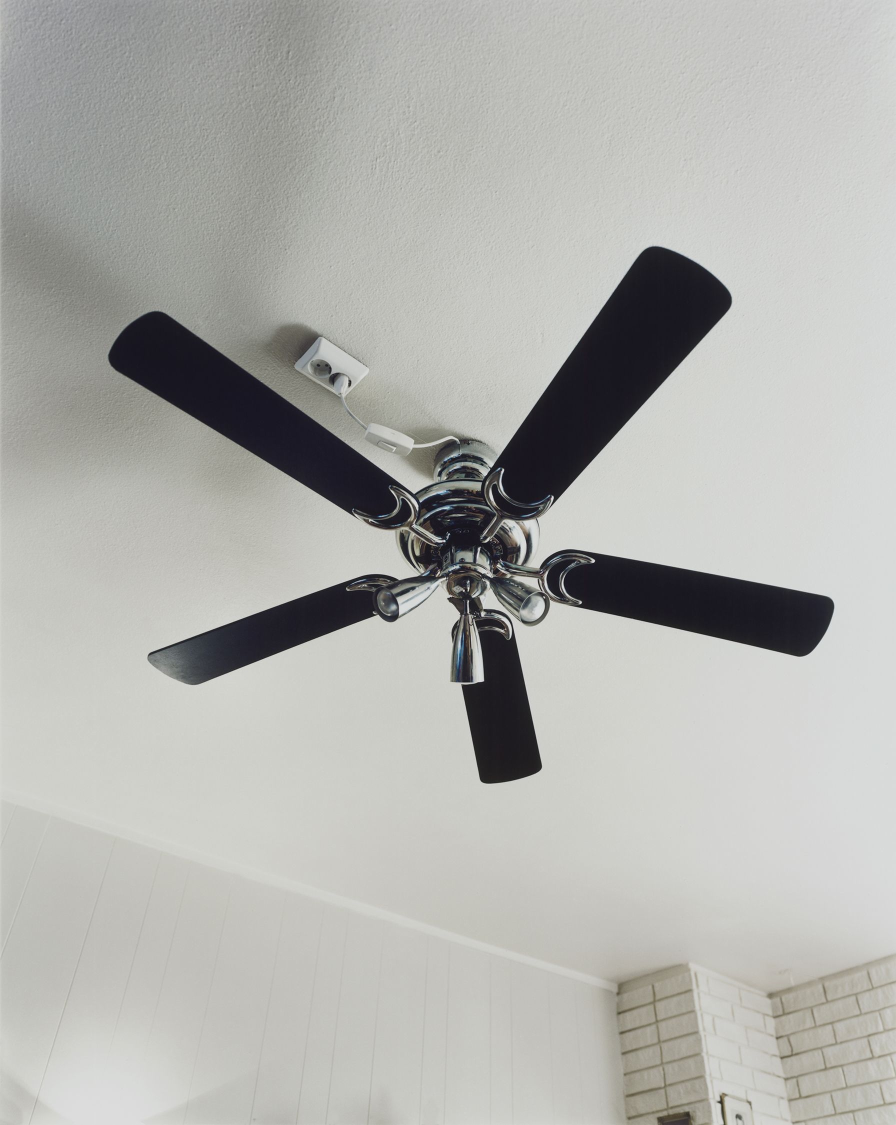 A ceiling fan with five black blades and a central light fixture, mounted on a white ceiling.