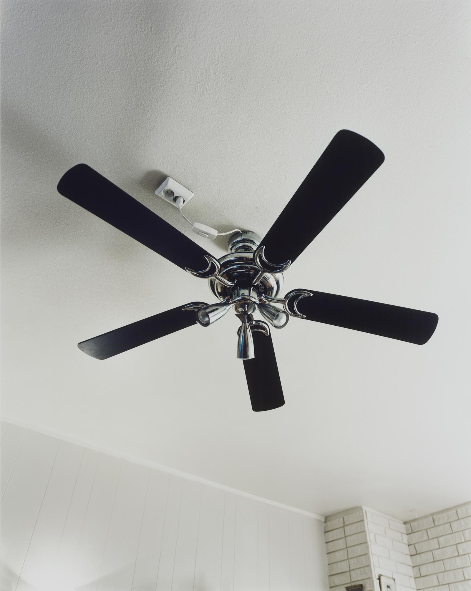 A ceiling fan with five black blades and a central light fixture, mounted on a white ceiling.