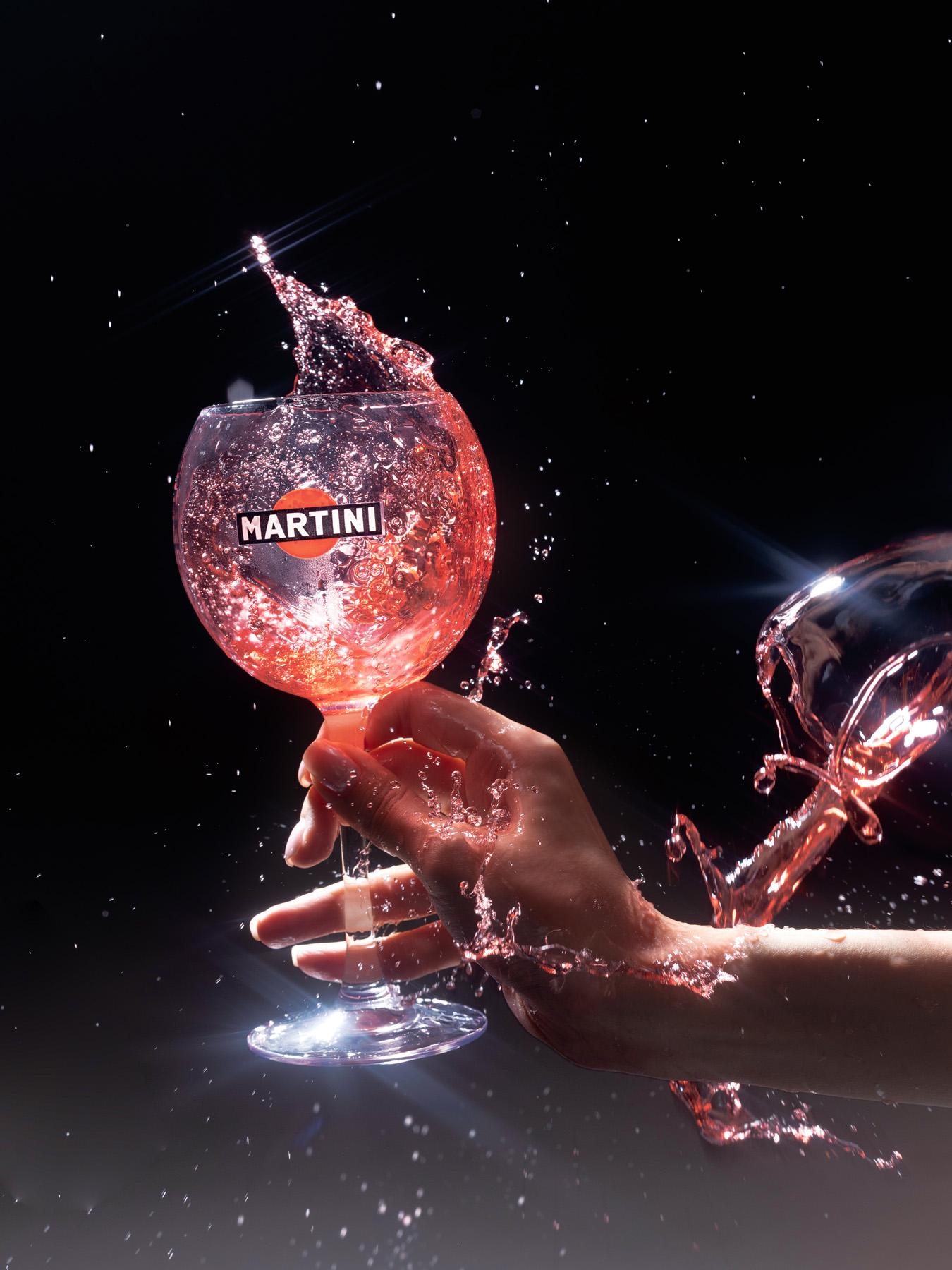 A glass of Martini cocktail being poured with a splash of liquid.