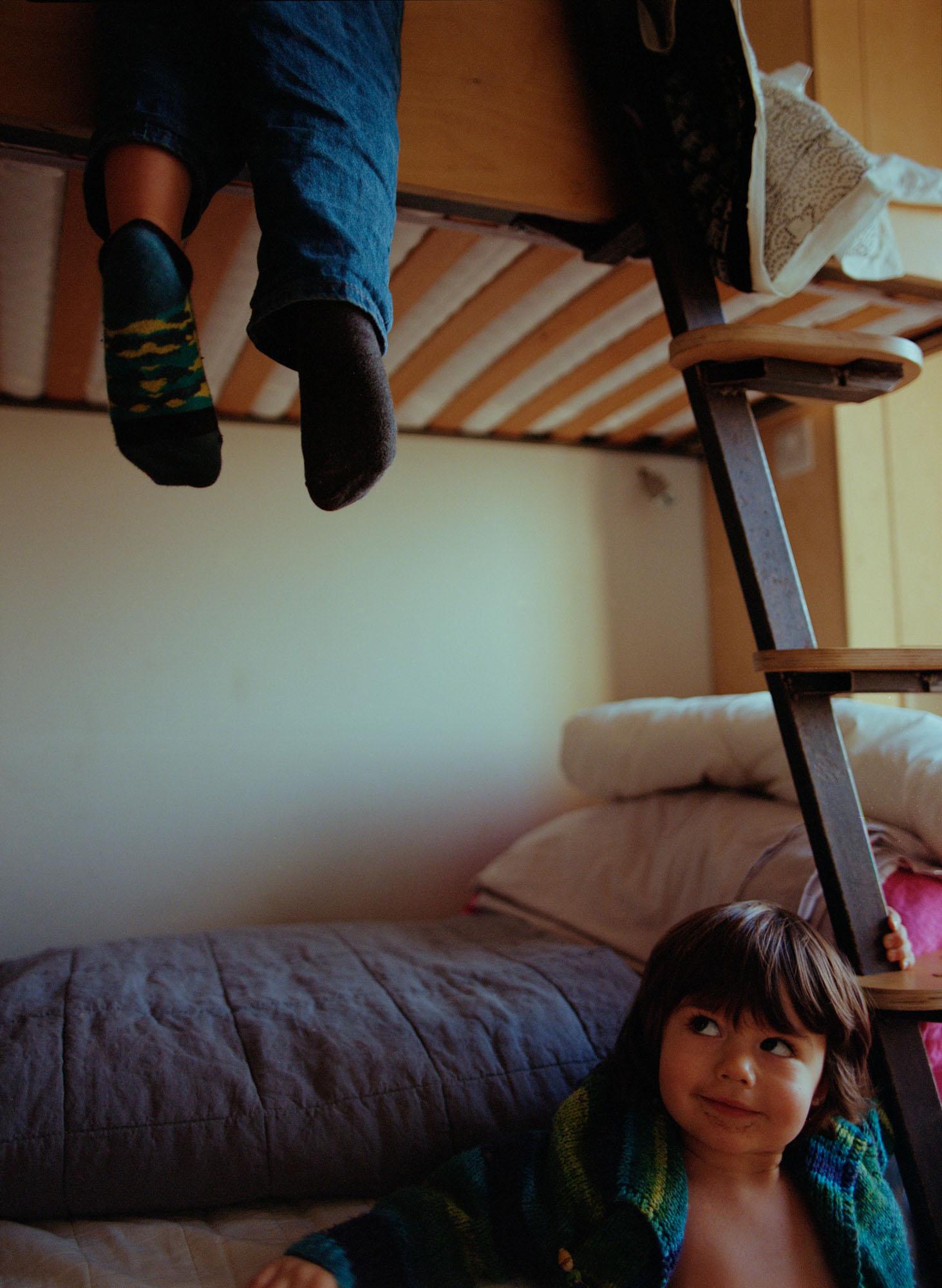 A person's legs are hanging from a bunk bed, wearing blue jeans and green and yellow striped socks.