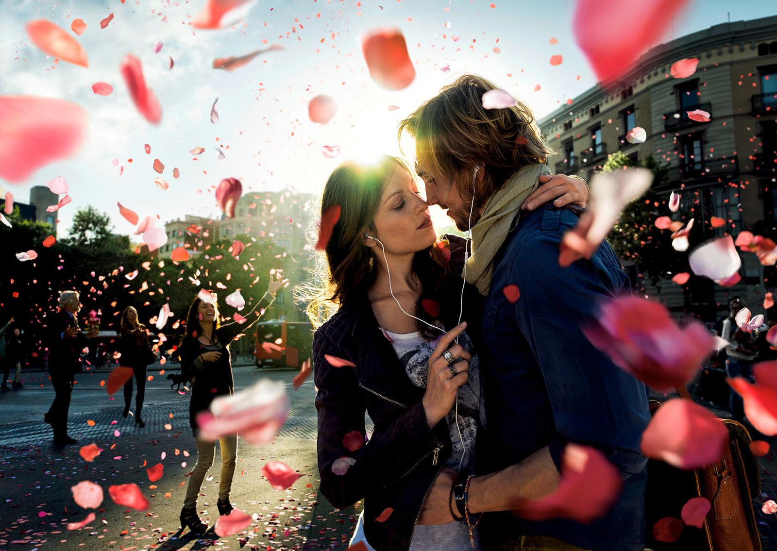 A young couple embracing in a city square, surrounded by falling rose petals.