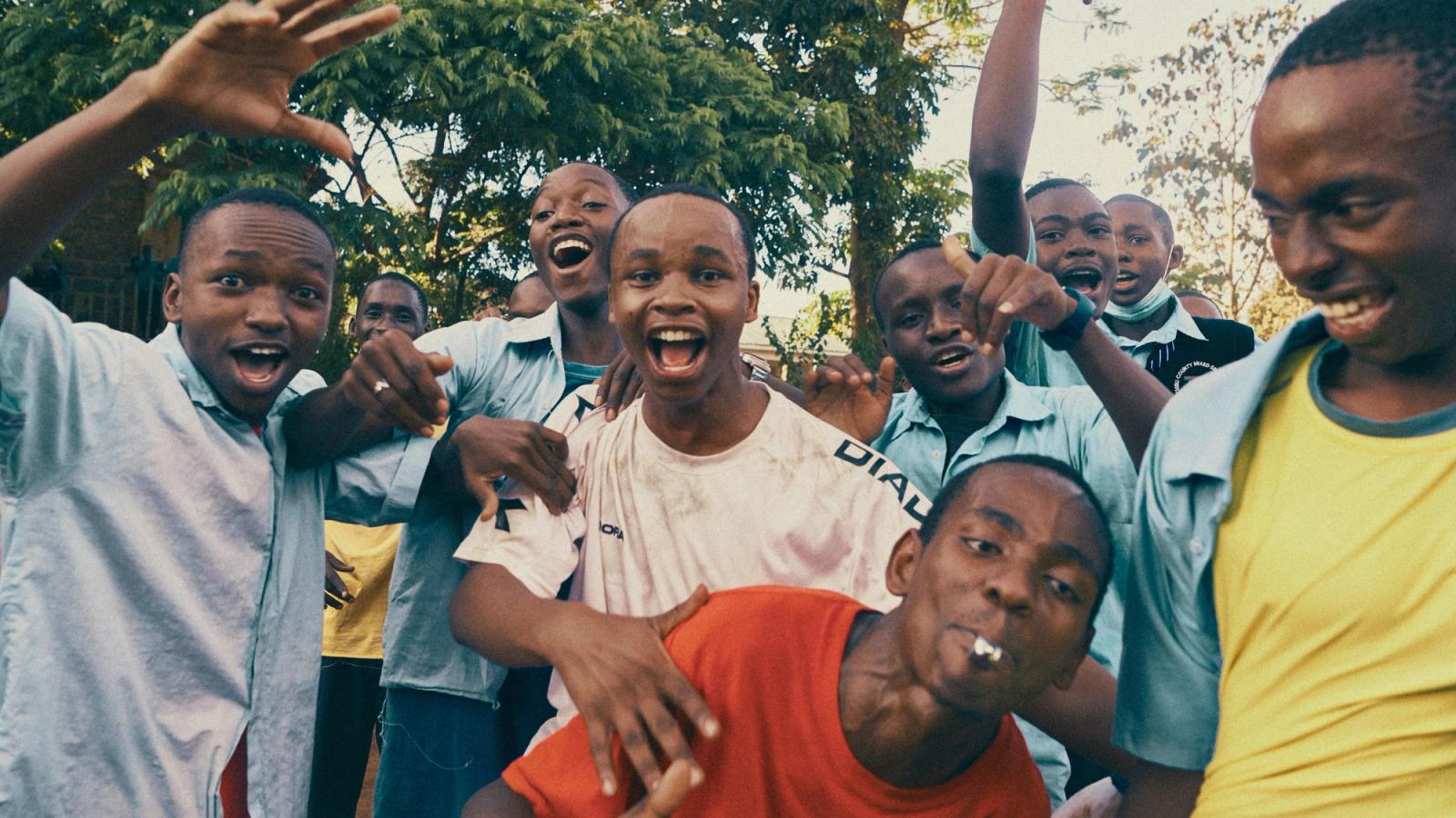 A group of young boys, likely students, are gathered together, smiling and laughing, with some of them making hand gestures or posing for the camera.