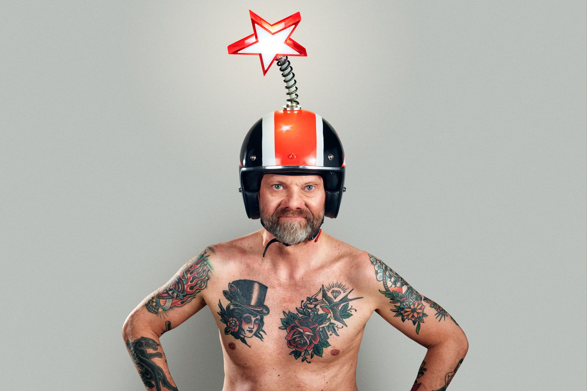 A man with tattoos and a beard wearing a helmet with a star on top, posing with his hands on his hips.
