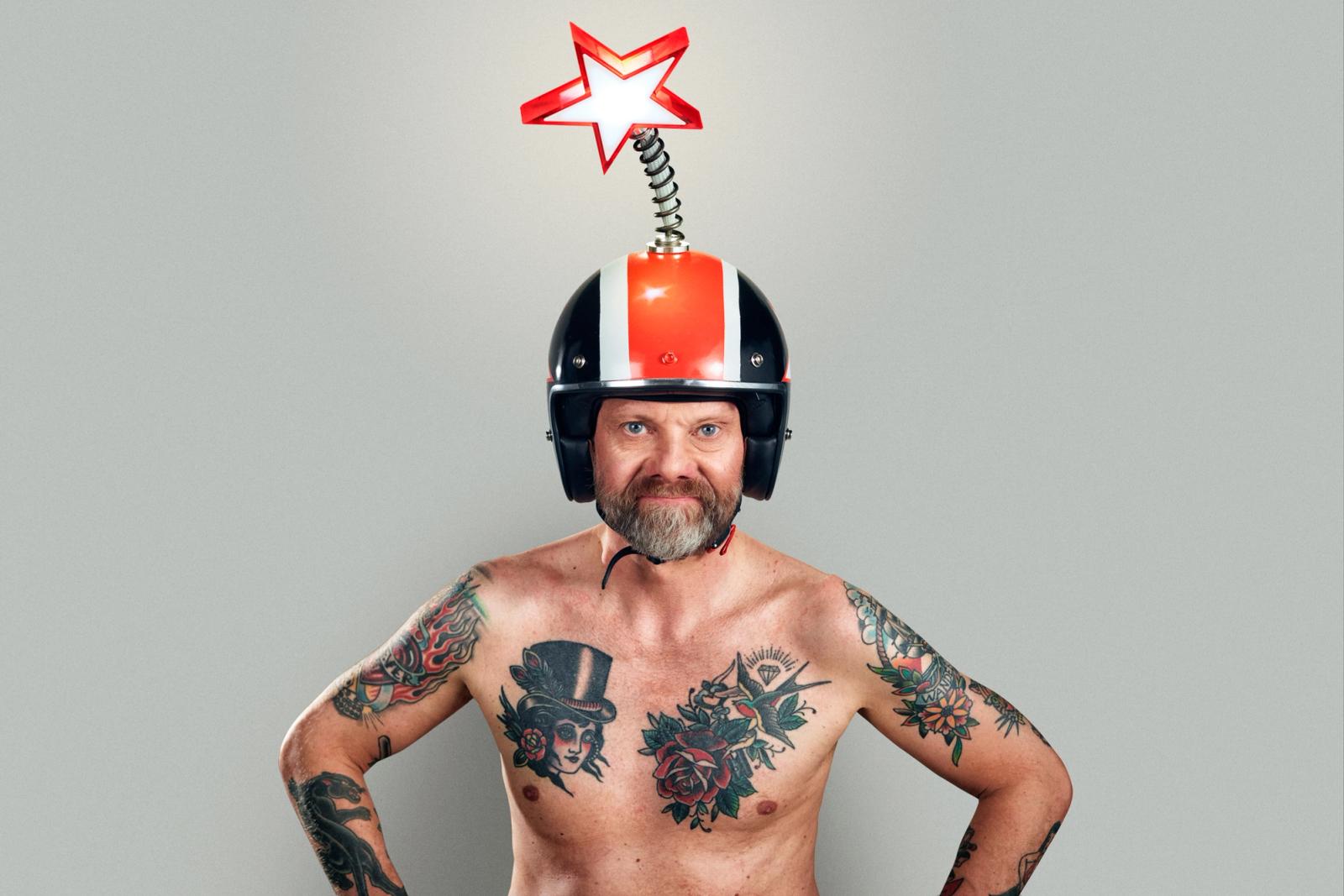 A man with tattoos and a beard wearing a helmet with a star on top, posing with his hands on his hips.