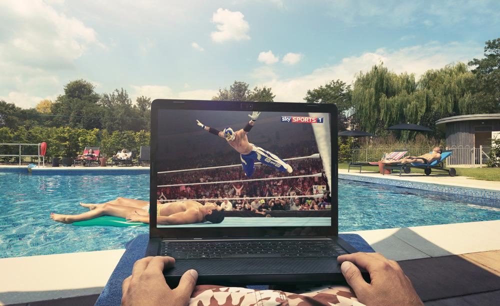 A person is sitting by a pool, watching a wrestling match on a laptop.