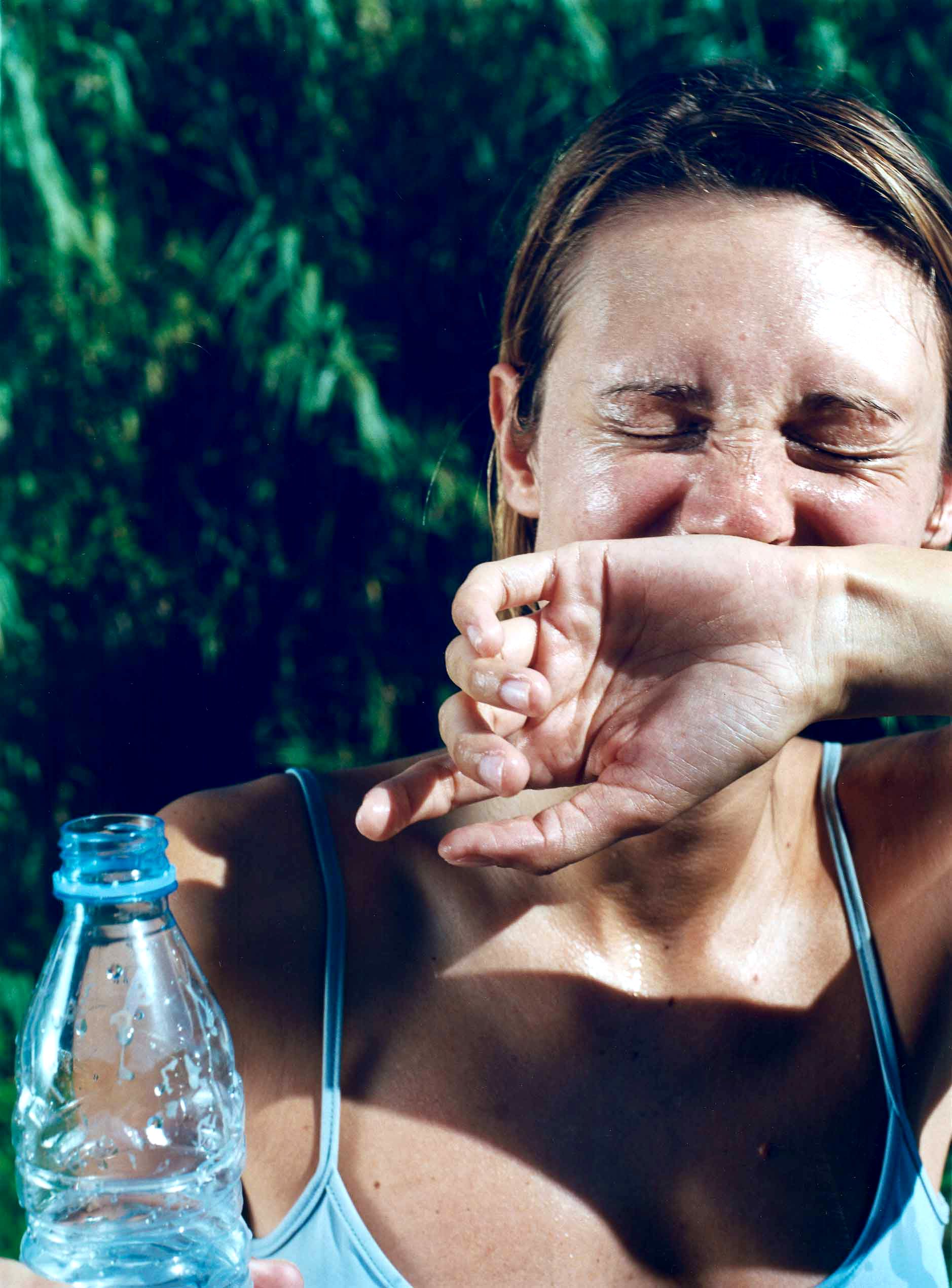 A woman is crying and covering her face with her hands, with a bottle of water in the foreground.
