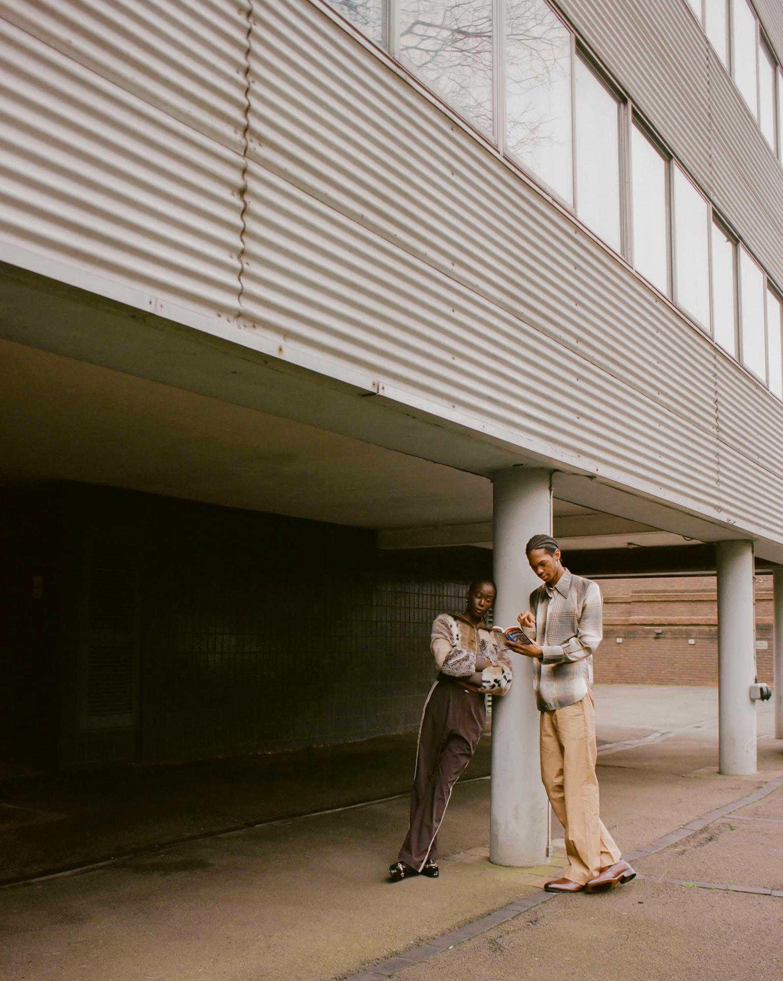 Two people standing in front of a building, each wearing casual clothing, with one holding a tablet.