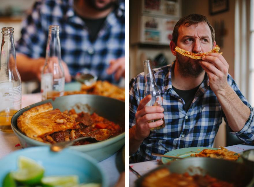 A man in a blue and white checkered shirt is eating a slice of pizza and holding a beer bottle.