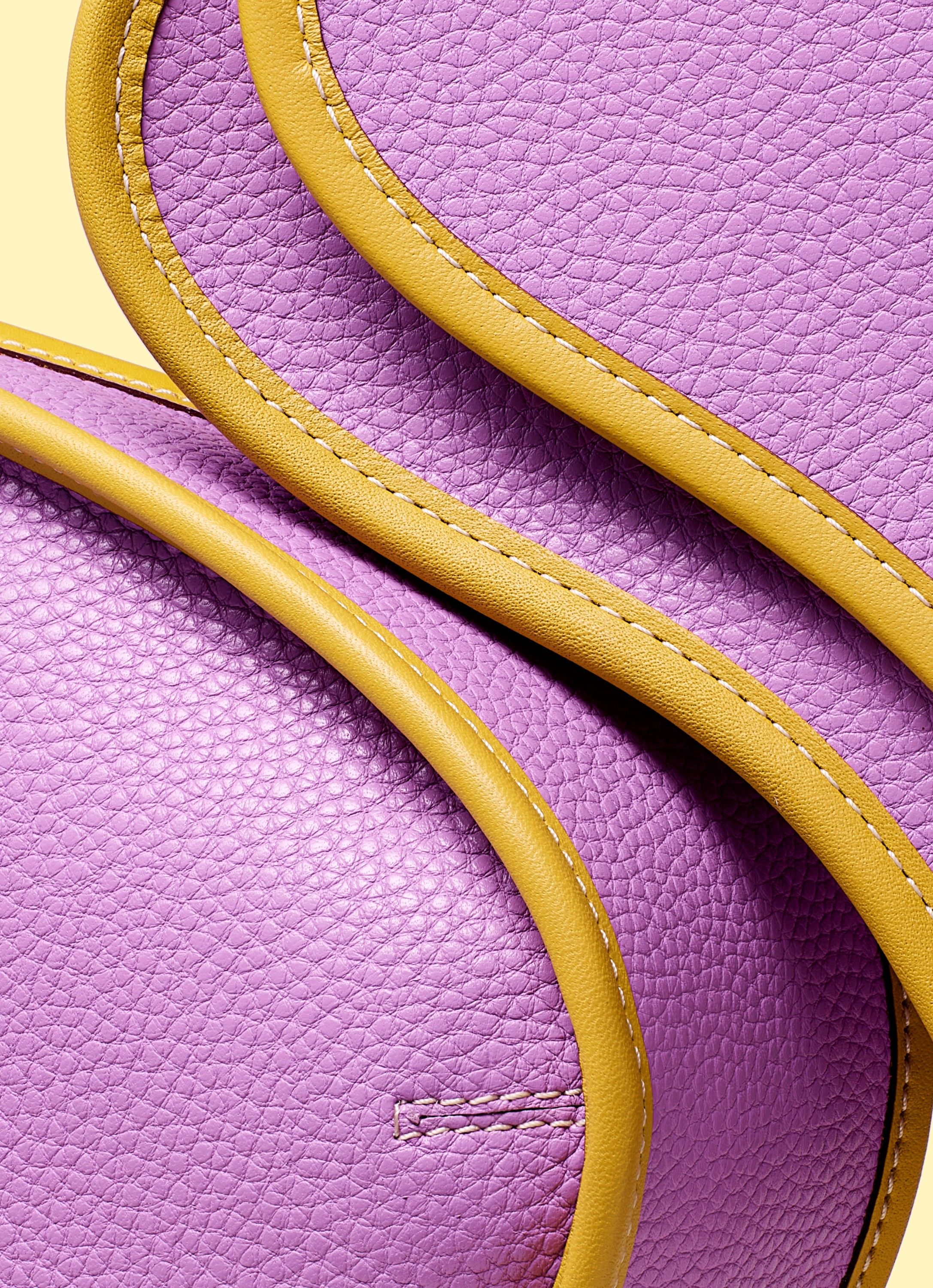 A close-up of a purple leather handbag with yellow leather trim and stitching.