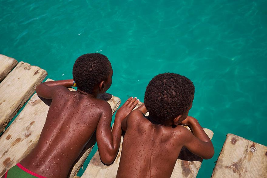 Two young boys, likely brothers, are lying on a wooden dock, looking out at the water.