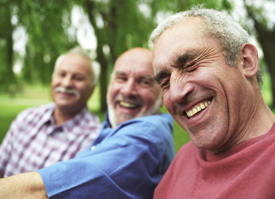 Three older men laughing and smiling in a park.