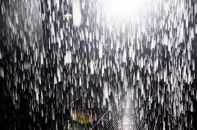 A large, dark, rain-filled room with water droplets falling from the ceiling, creating a misty atmosphere.