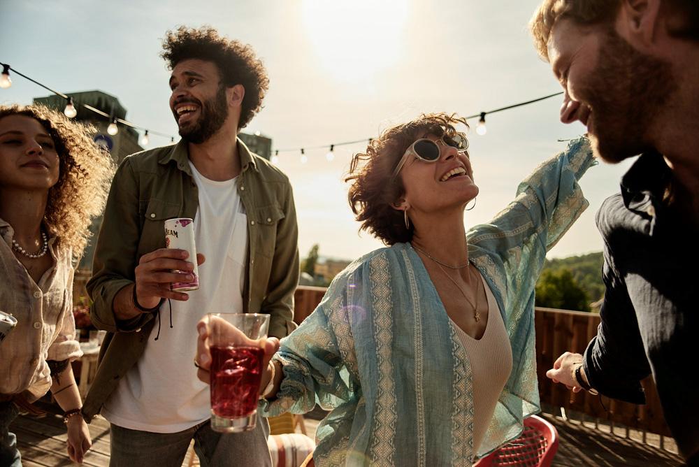 A group of people enjoying drinks on a rooftop with a city skyline visible.