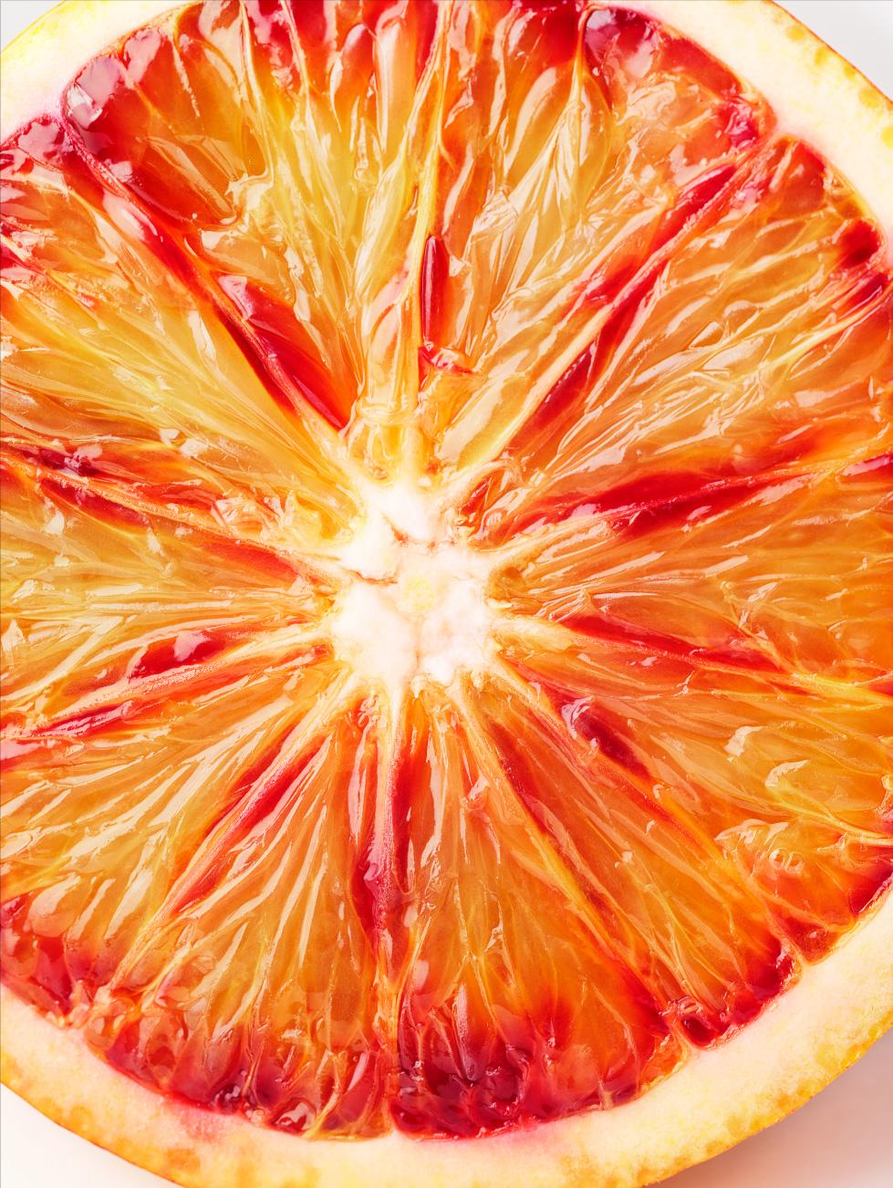 A close-up of a juicy, orange-red, blood orange slice, with visible, juicy, orange-red, pulp and a few, small, white, pithy, seeds.