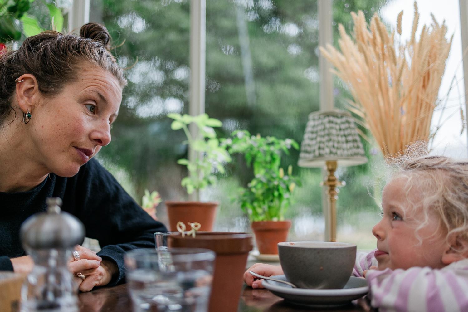 A woman and a young girl sitting at a table, sharing a moment with mixed expressions.
