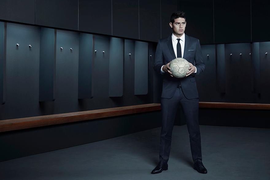 A man in a suit and tie holding a soccer ball in a dimly lit, empty locker room.