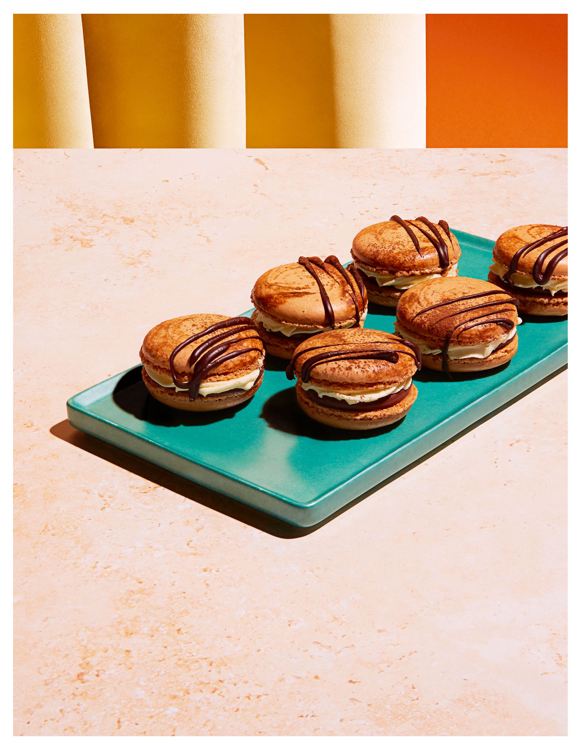A selection of chocolate macarons on a green plate, with a few of them having a chocolate drizzle on top.
