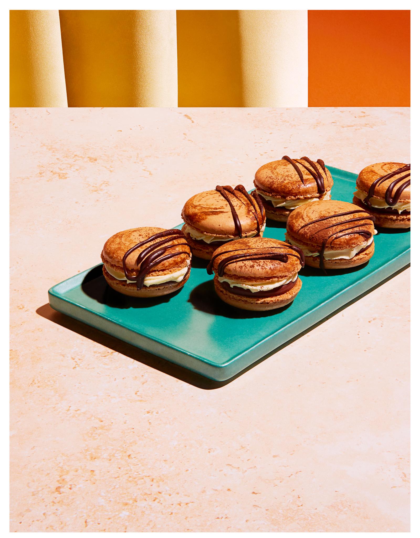 A selection of chocolate macarons on a green plate, with a few of them having a chocolate drizzle on top.