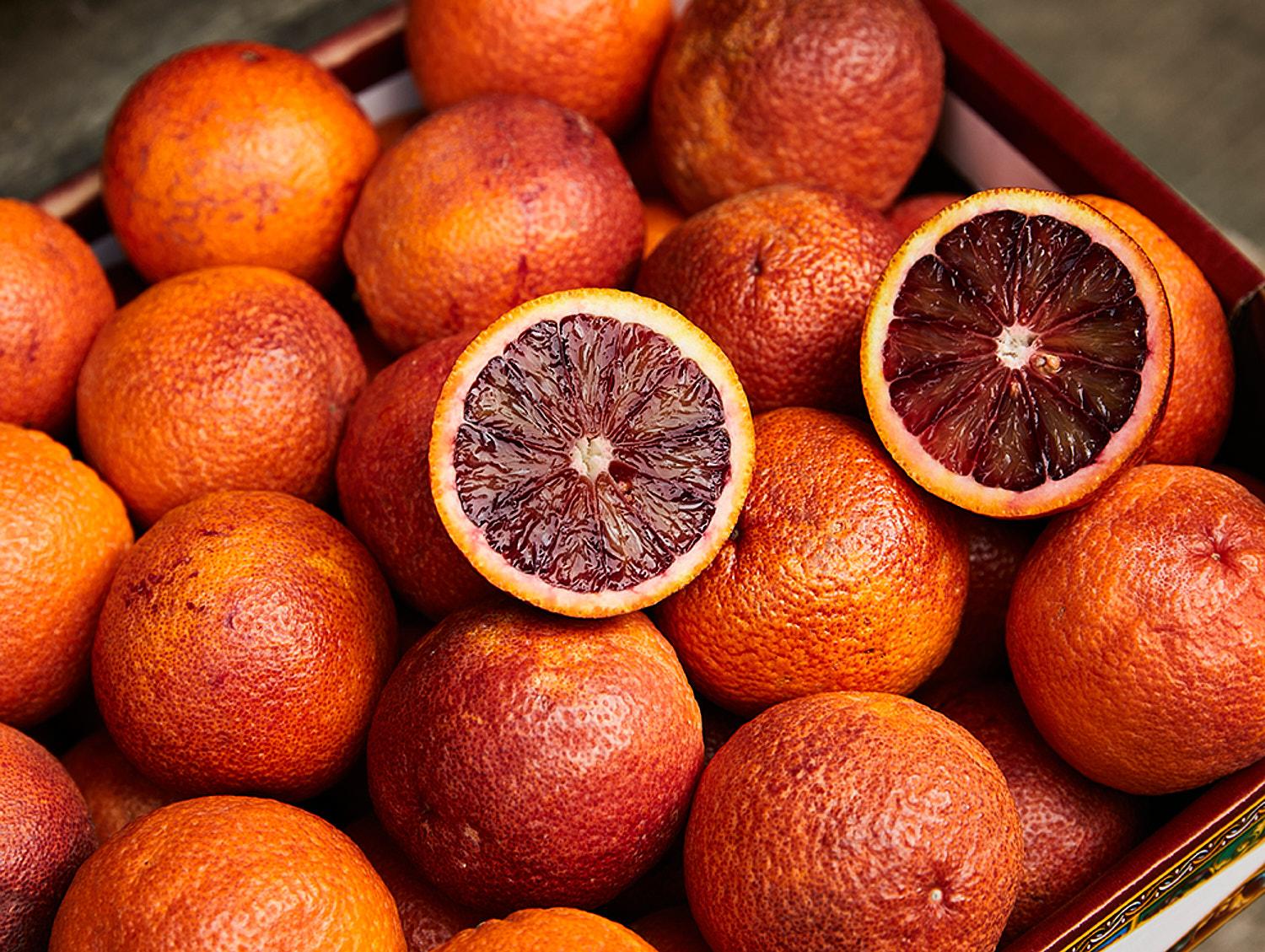 A red ceramic dish filled with blood oranges, some halved to reveal the pink interior.
