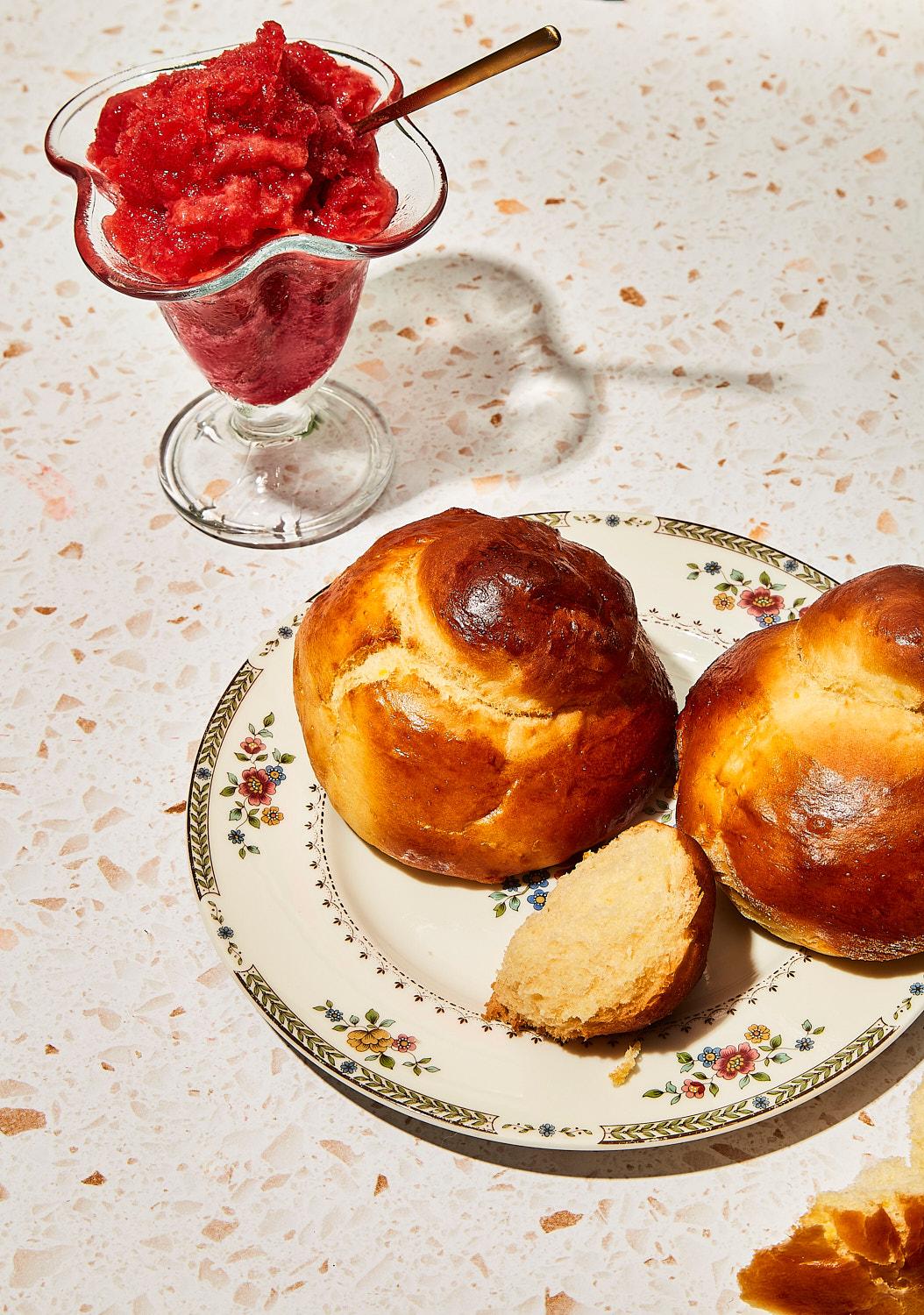 A glass cup with a red dessert and two golden pastries on a white and pink speckled surface.