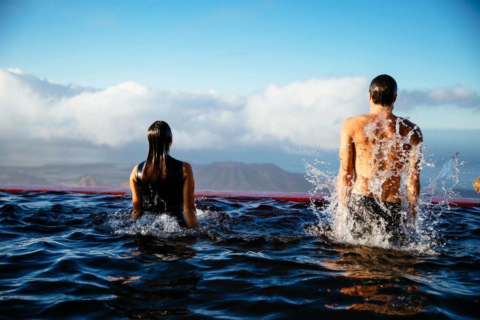 Two people in the ocean, one man and one woman, both wearing wetsuits.
