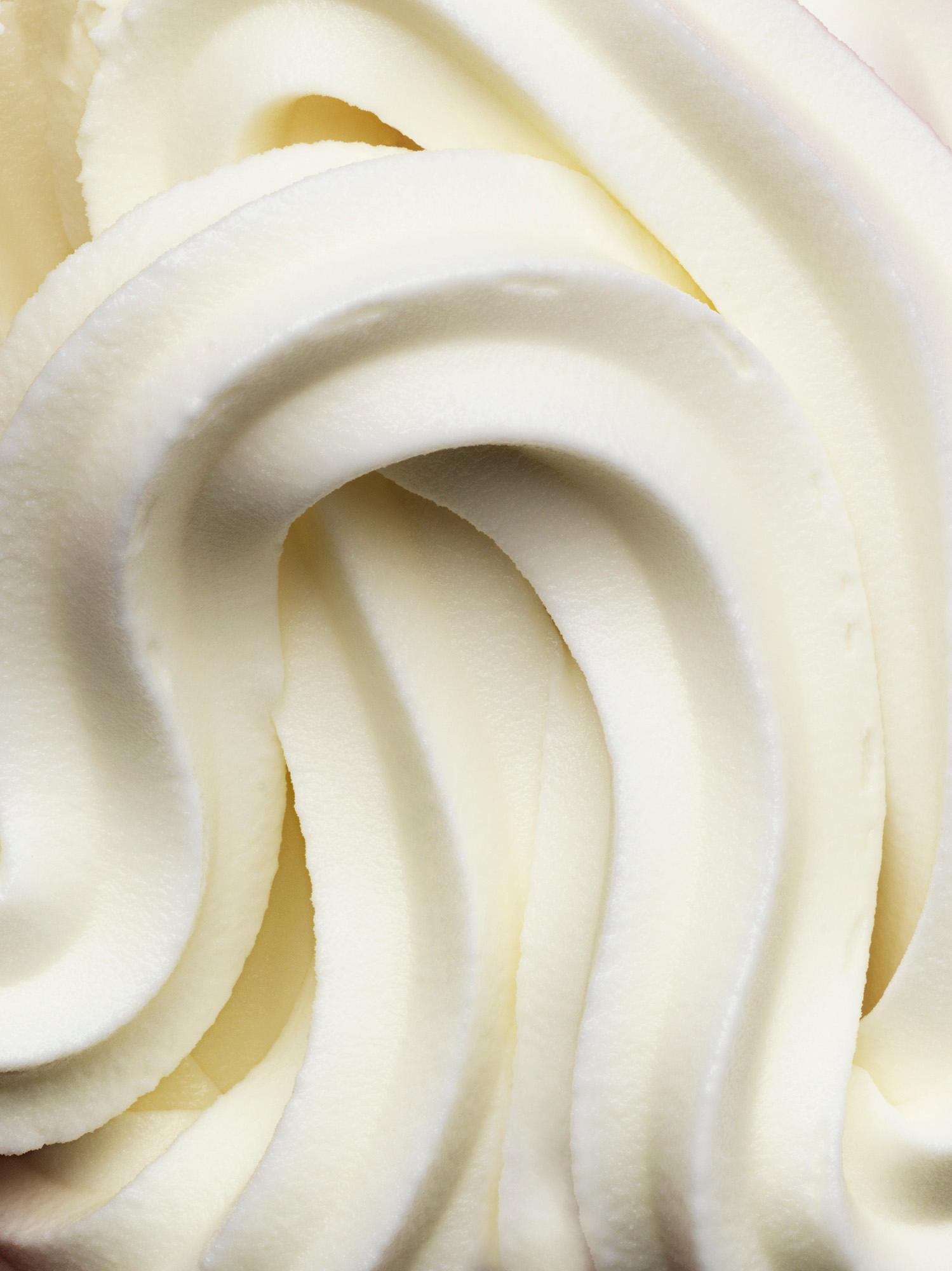 This close-up image of a creamy white substance, likely whipped cream or butter, conveys a sense of indulgence and luxury. The smooth, velvety texture and gentle, curved patterns.