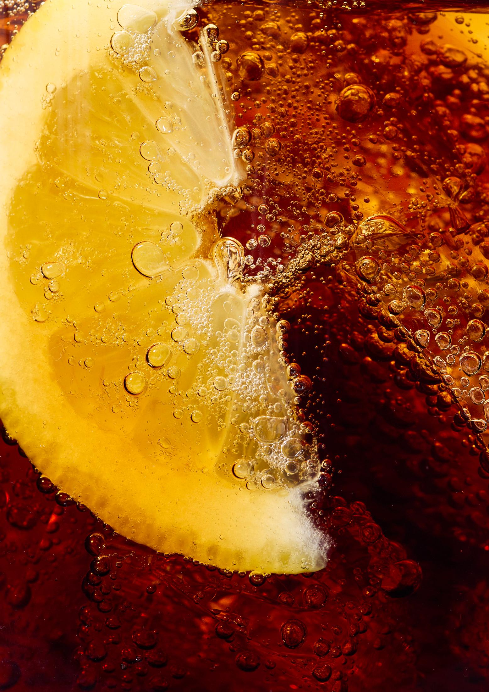 A close-up of a lemon slice in a glass of iced tea, with the lemon slice partially submerged in the liquid and surrounded by ice cubes.