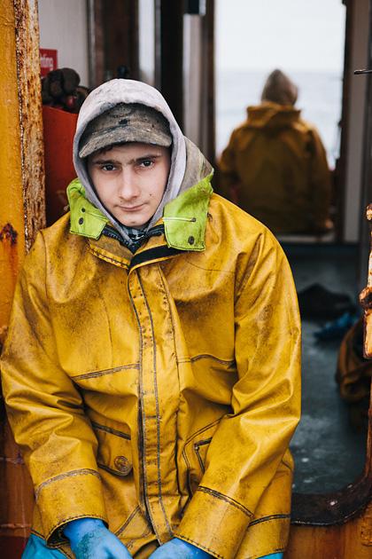 A young boy in a yellow raincoat and hat, standing in a doorway, looking directly at the camera.