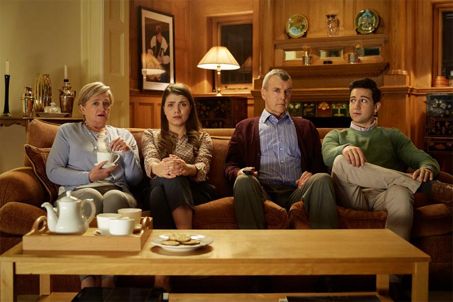 Four people sitting on a couch in a living room, with a coffee table in front of them.