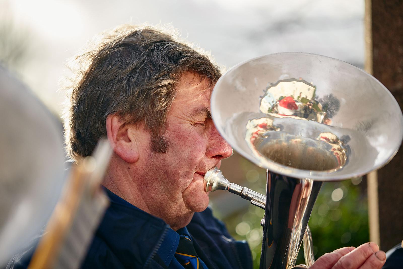 A man playing a trumpet, wearing a blue jacket and a tie, with a blurred background.