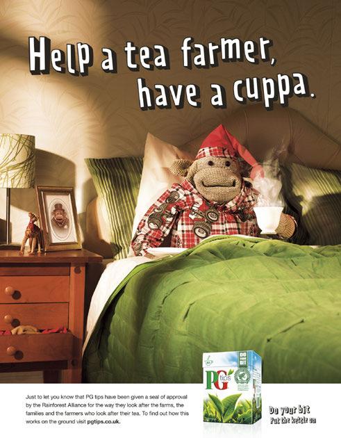 A bed with a monkey wearing a red and white plaid nightgown and a red hat, holding a cup of tea.