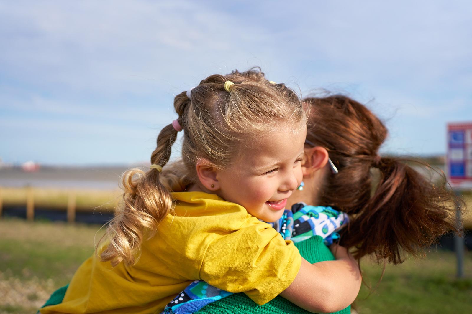 A young girl in a yellow t-shirt and a woman in a green sweater embracing in a field.