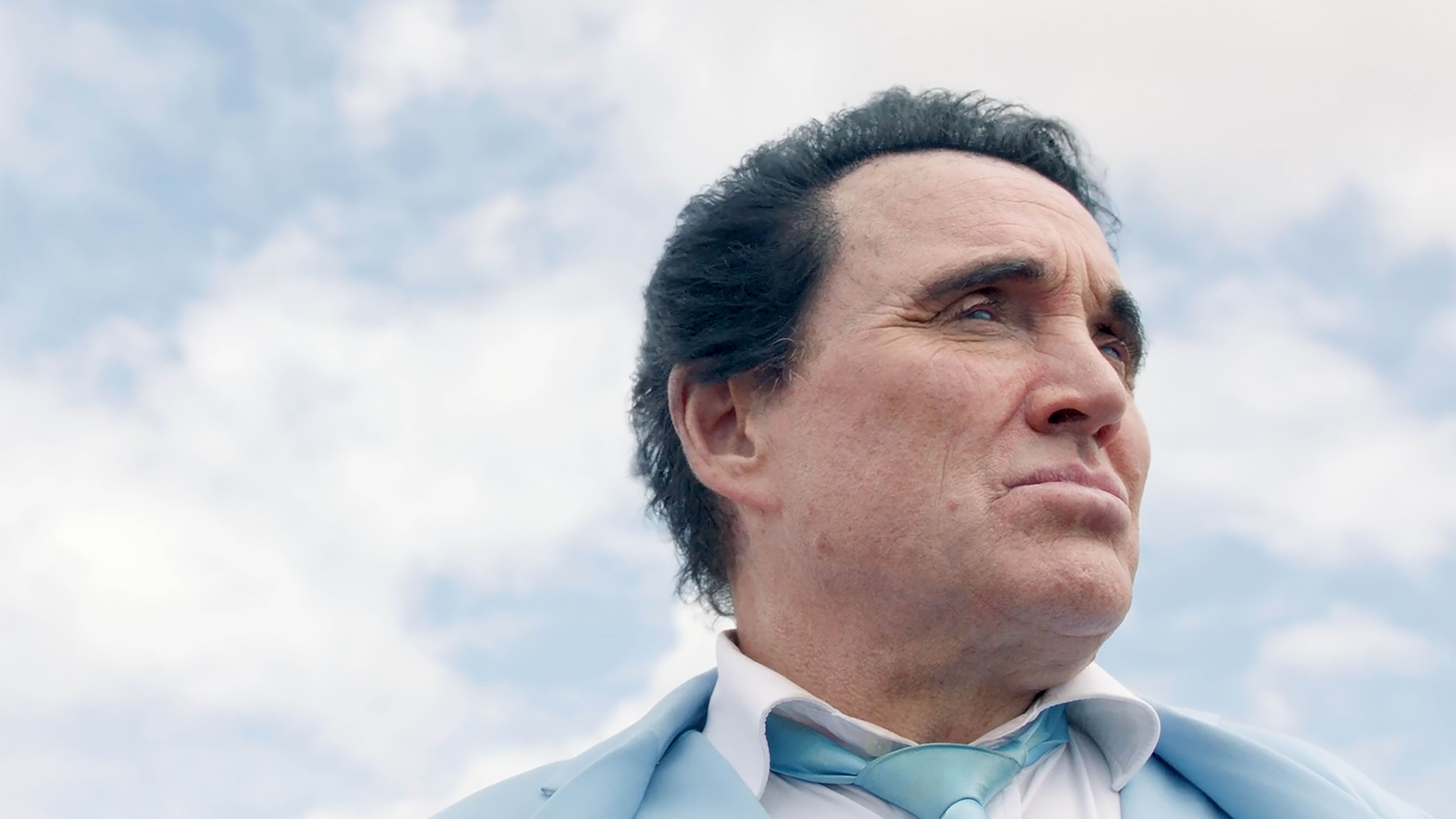 Callum O'Keefe Still from JUAN film, about elvis impersonator blue suit looking sad and pensive in front of blue sky
