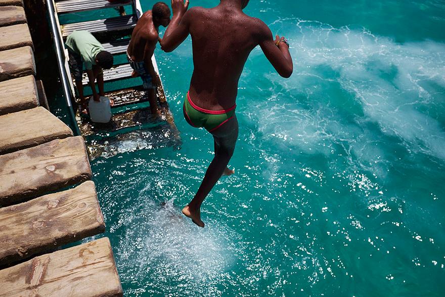 A person in a green and pink swimsuit is jumping into the water from a dock.