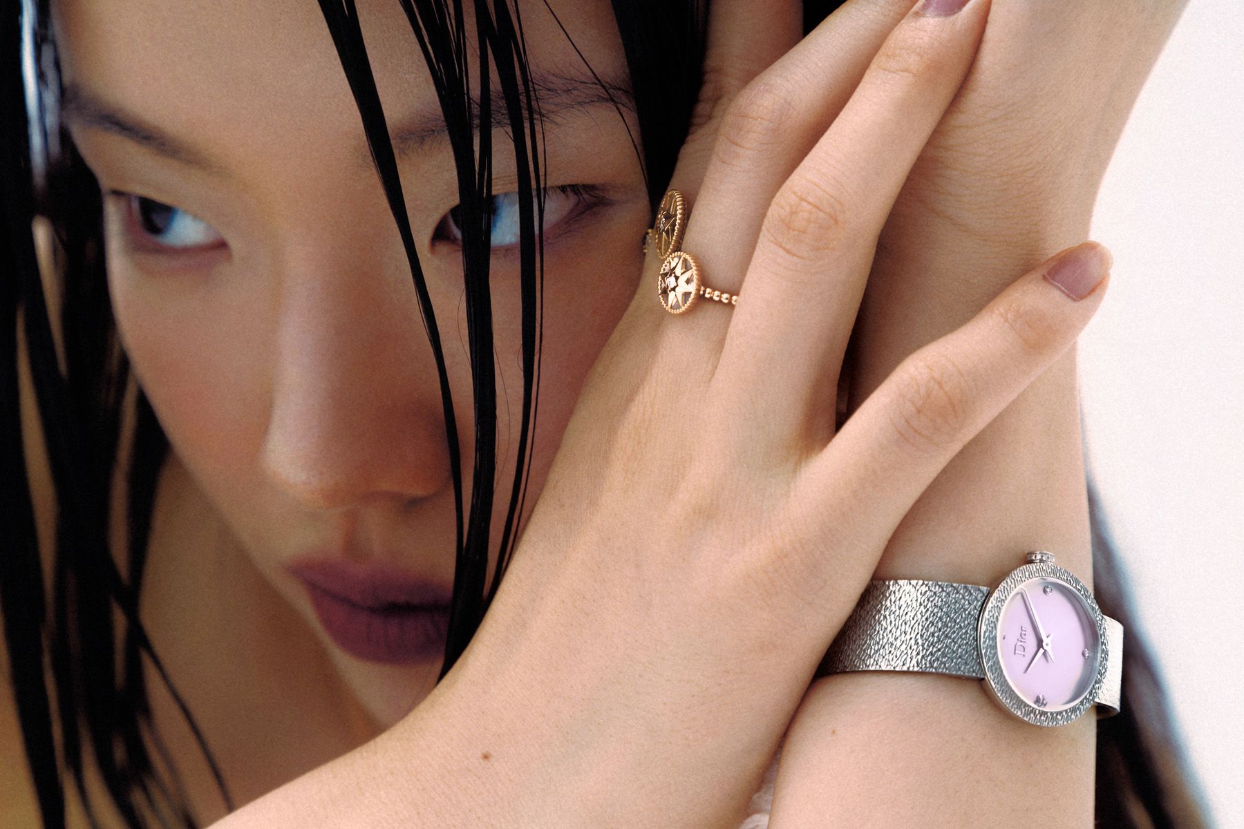 A woman with long, dark hair and a silver watch on her wrist, wearing a white shirt and a silver necklace with a pendant.