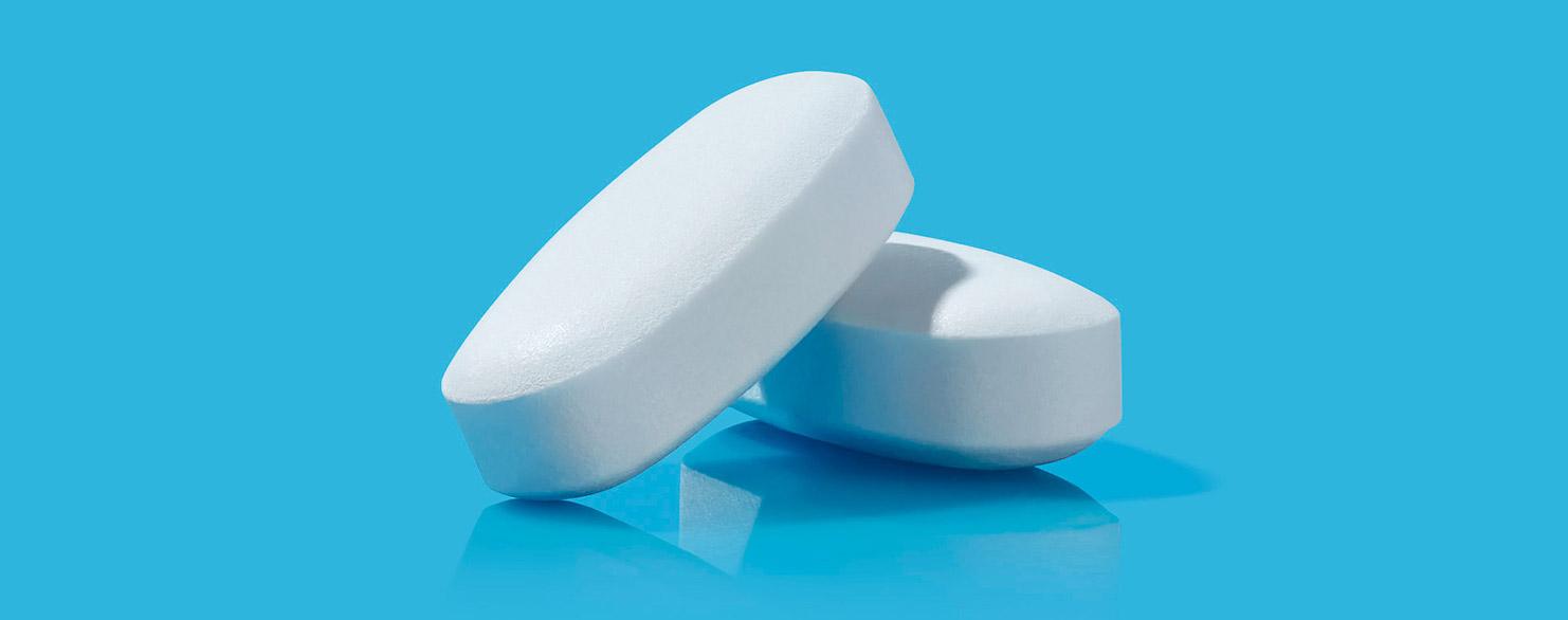 Two white, oval-shaped pills on a blue background.