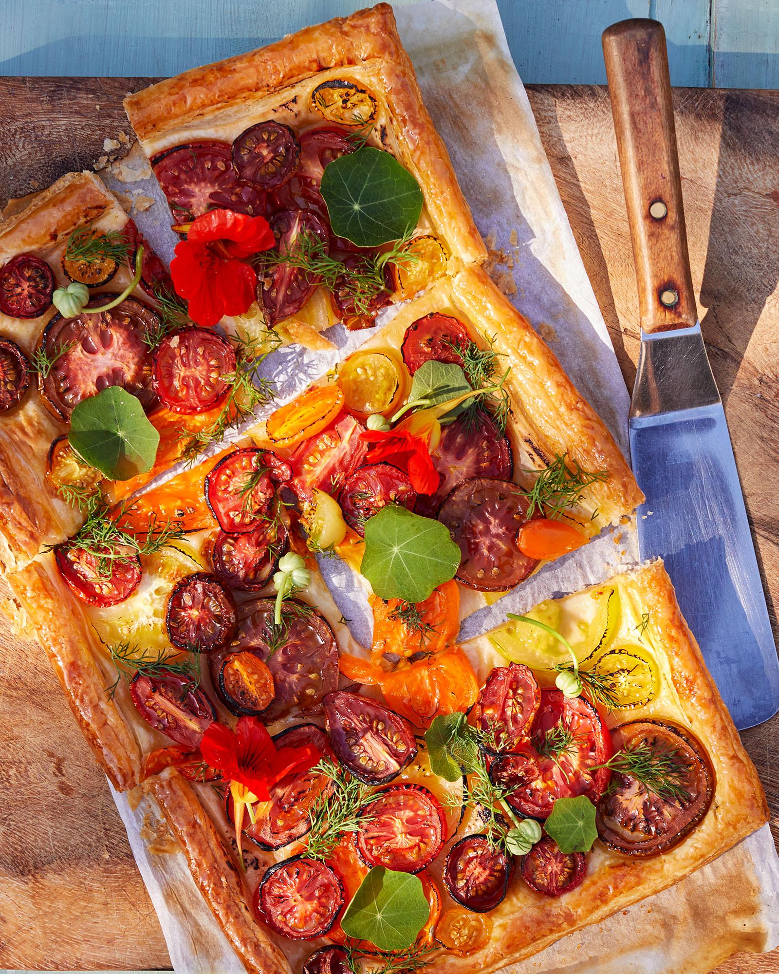 A rectangular, flaky pastry filled with roasted tomatoes, herbs, and cheese, cut into multiple pieces.