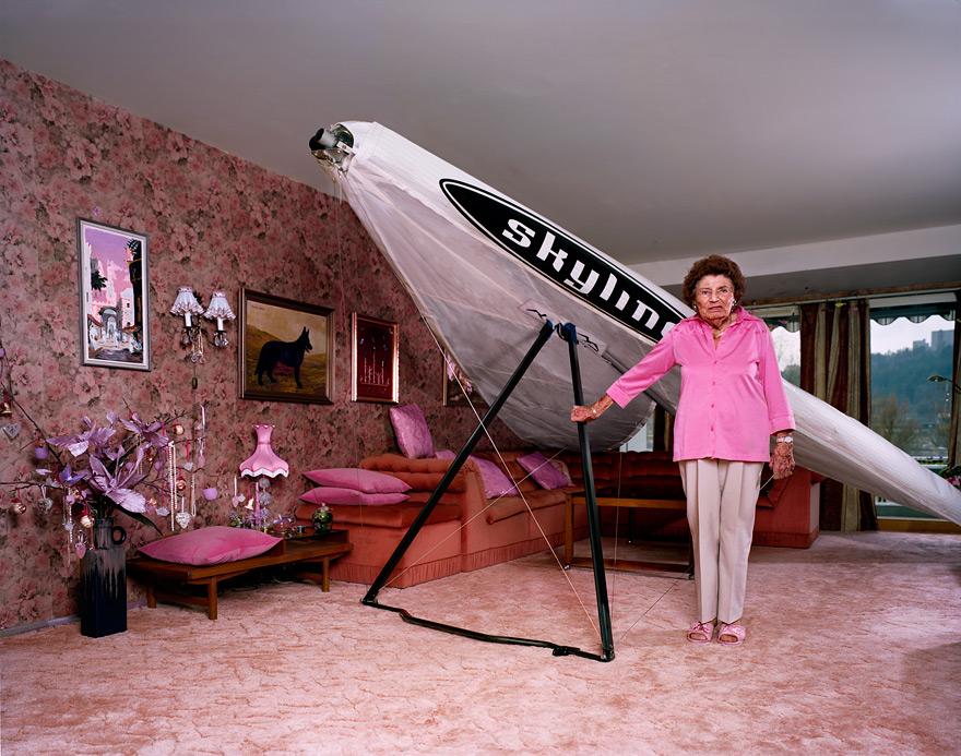 A woman in a pink shirt and beige pants stands in front of a large, white, inflatable SkyMall airship in a living room with pink and white furniture and decorations.
