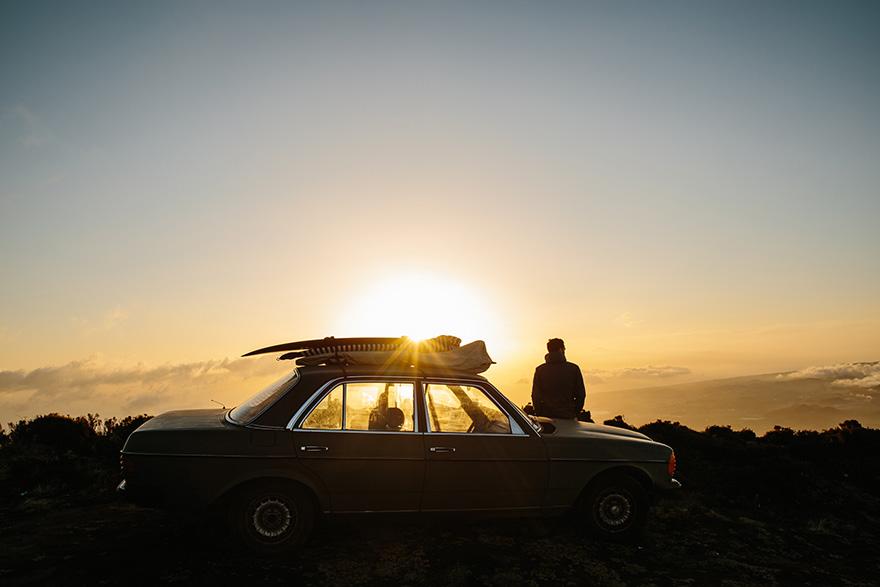 A person is sitting on the roof of a car, looking out at a beautiful sunset.
