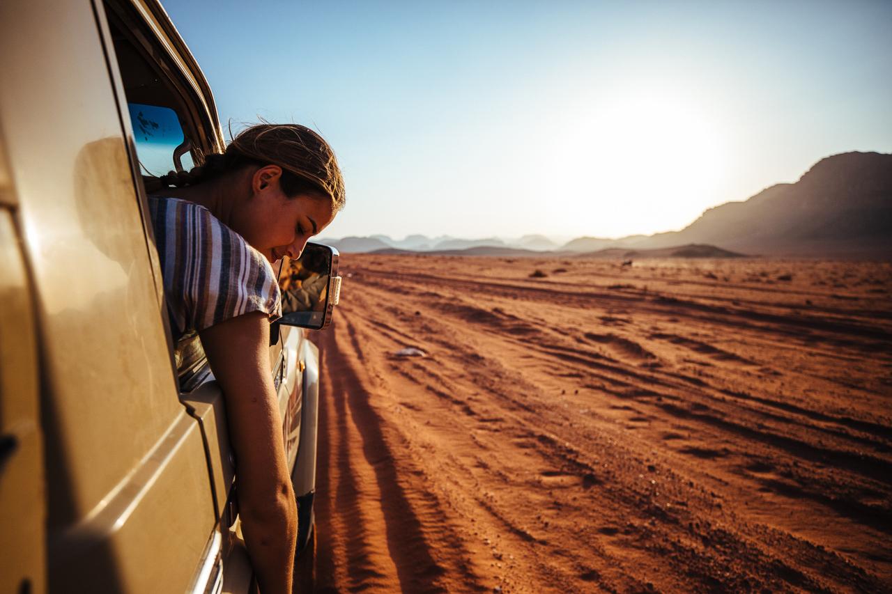 A woman leaning out of a car window in the middle of a desert landscape, wearing a striped t-shirt.