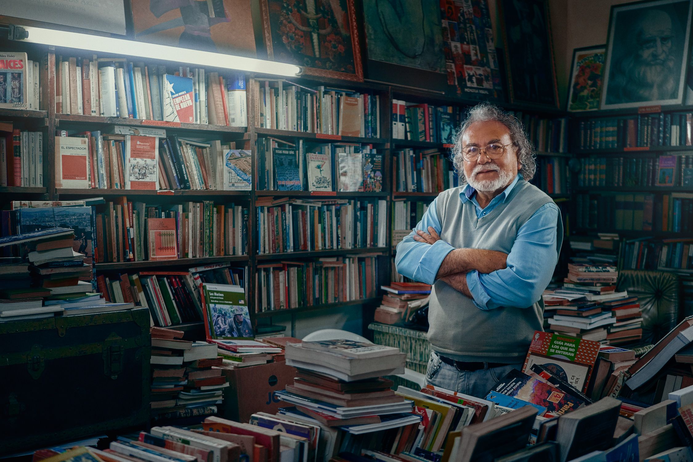 A man stands in a room filled with books and art, arms crossed.