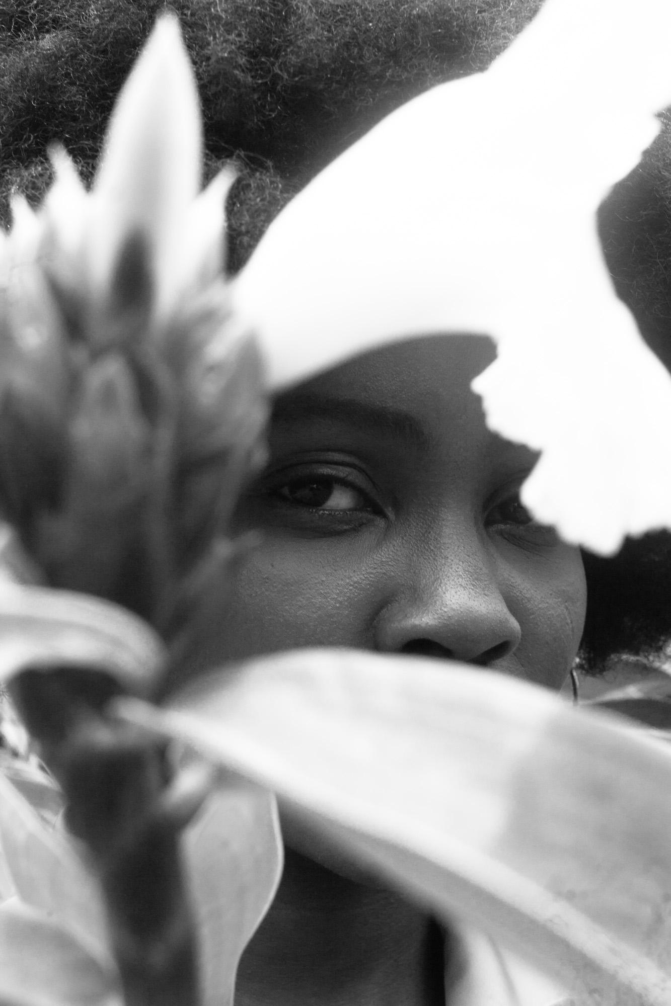A close-up of a woman’s face partially obscured by a large leafy plant.