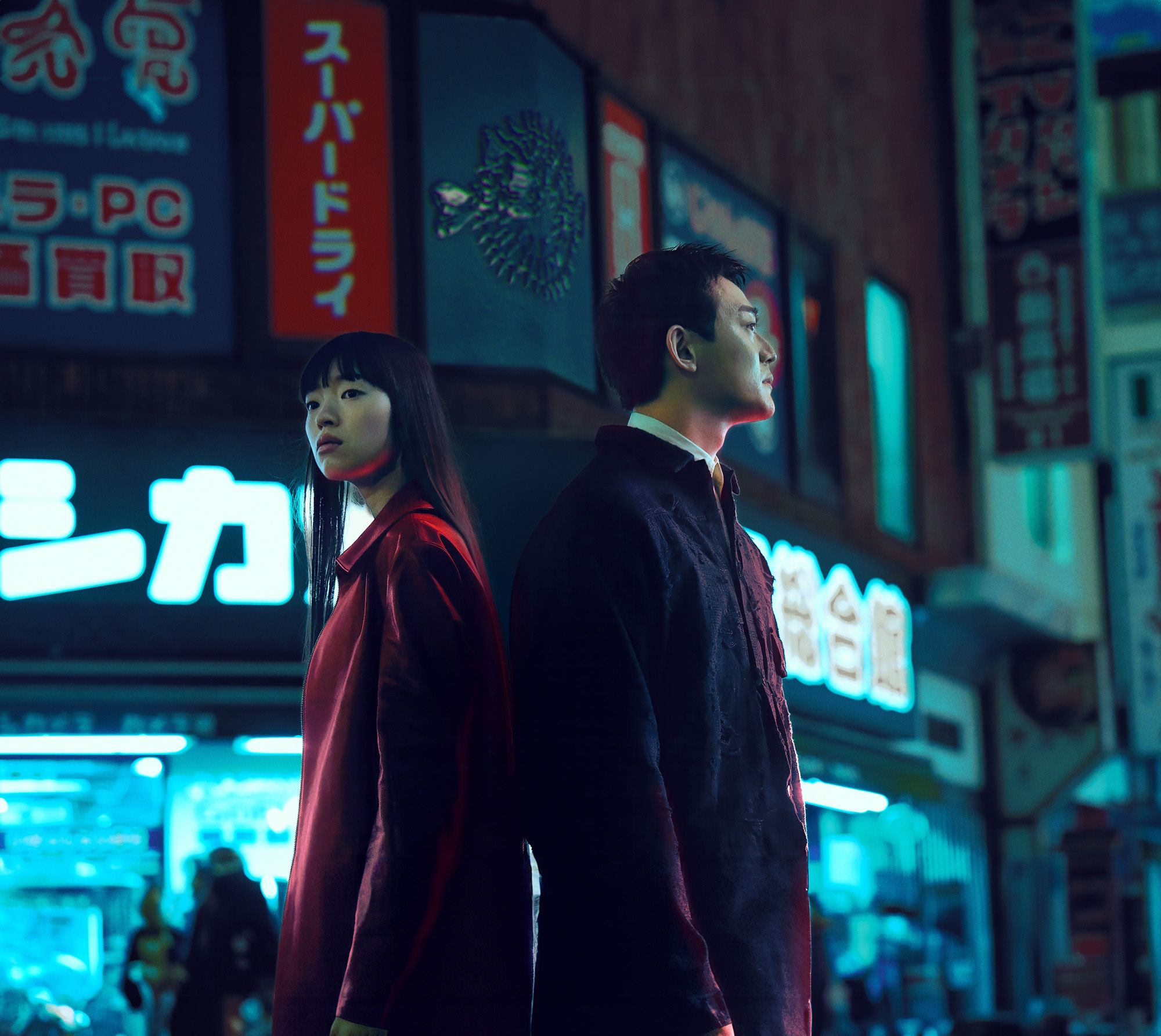 A man and a woman standing back-to-back, looking out over a city at night.